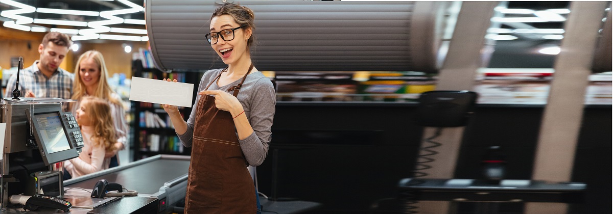 Portrait of smiling woman cashier pointing finger at an open sign while standing at cash counter in supermarket